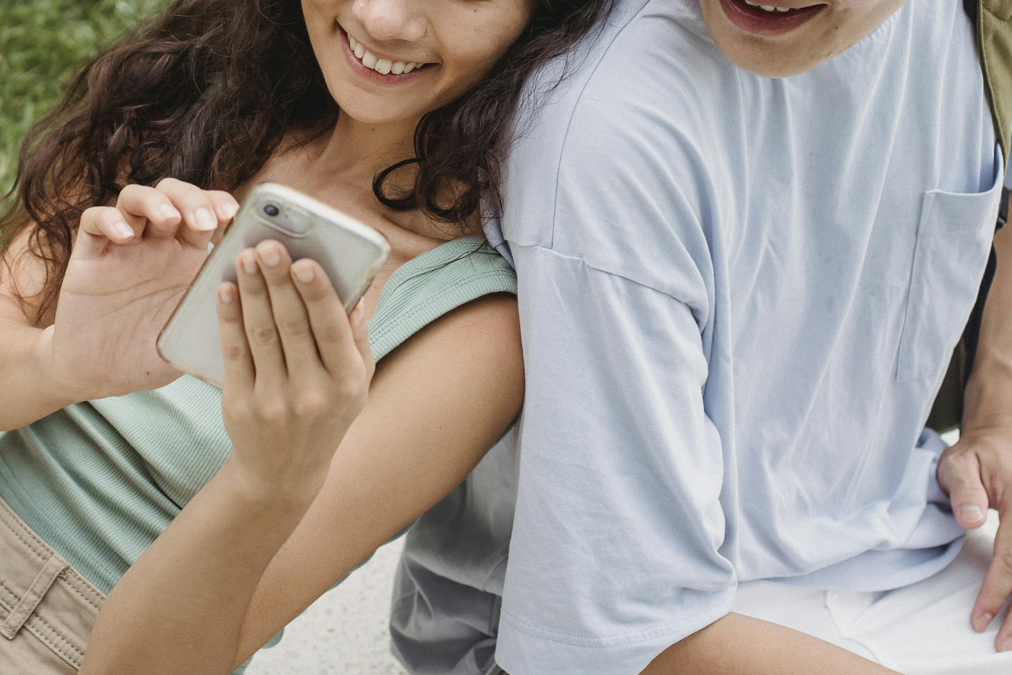 From above of crop anonymous happy couple sharing mobile phone while resting on city bench in summer